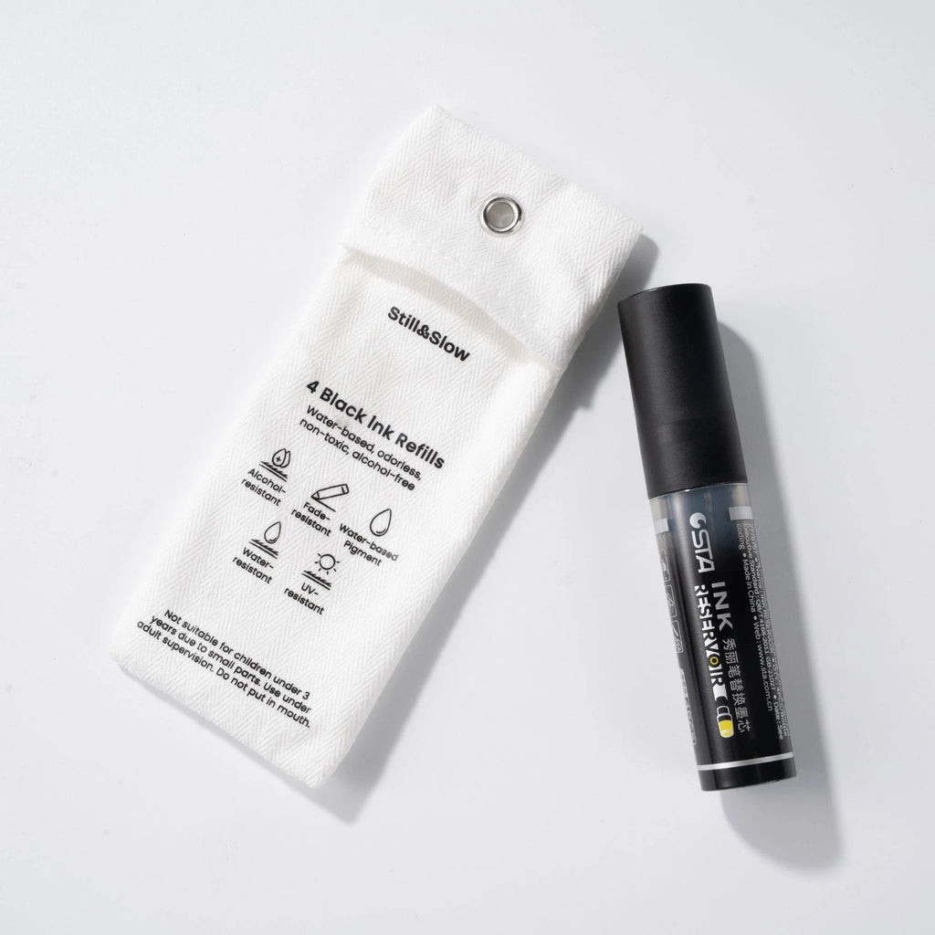 Black ink refill tube beside its white paper packaging on a plain background